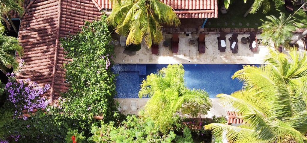 Vista aérea de la piscina de la casa principal del hotel Cuaca Viejo Fundadores. Es una piscina de aproximadamente dos metro de ancho por 10 metros de largo, tiene una pequeña zona destinada a hidromasajes. Alrededor de la psicina se encuentran sillas para tomar el sol.